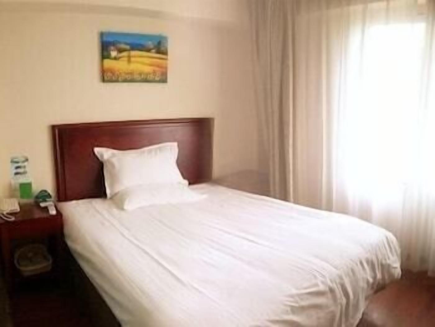 A hotel room with a single bed, a nightstand, a painting on the wall, and a window with curtains.