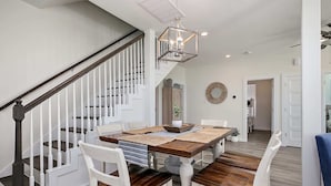 A dining area with a wooden table, white chairs, and a staircase with white railings.