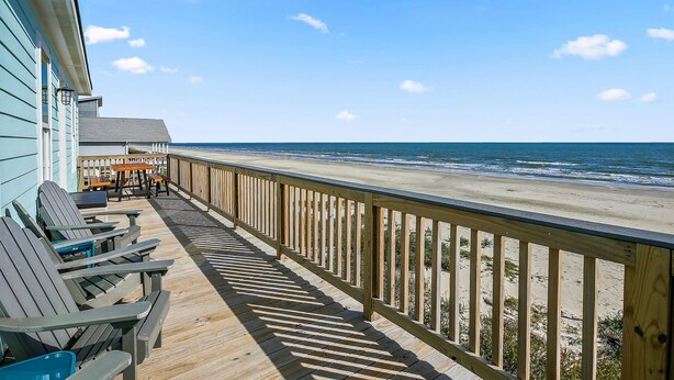 A wooden deck with chairs and tables overlooking a beach.