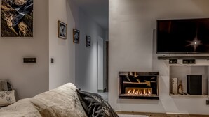 Ein modernes Wohnzimmer mit Kamin, einem flachbildfernseher an der Wand und einem gemütlichen Sofa mit gemusterten Kissen.