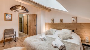 Ein Schlafzimmer mit Oberlicht, einem Bett mit aufgerollten Handtüchern, einem Sessel und einem Holz-Kopfteil.