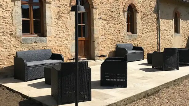 A stone building with arched windows and outdoor seating with wicker furniture.