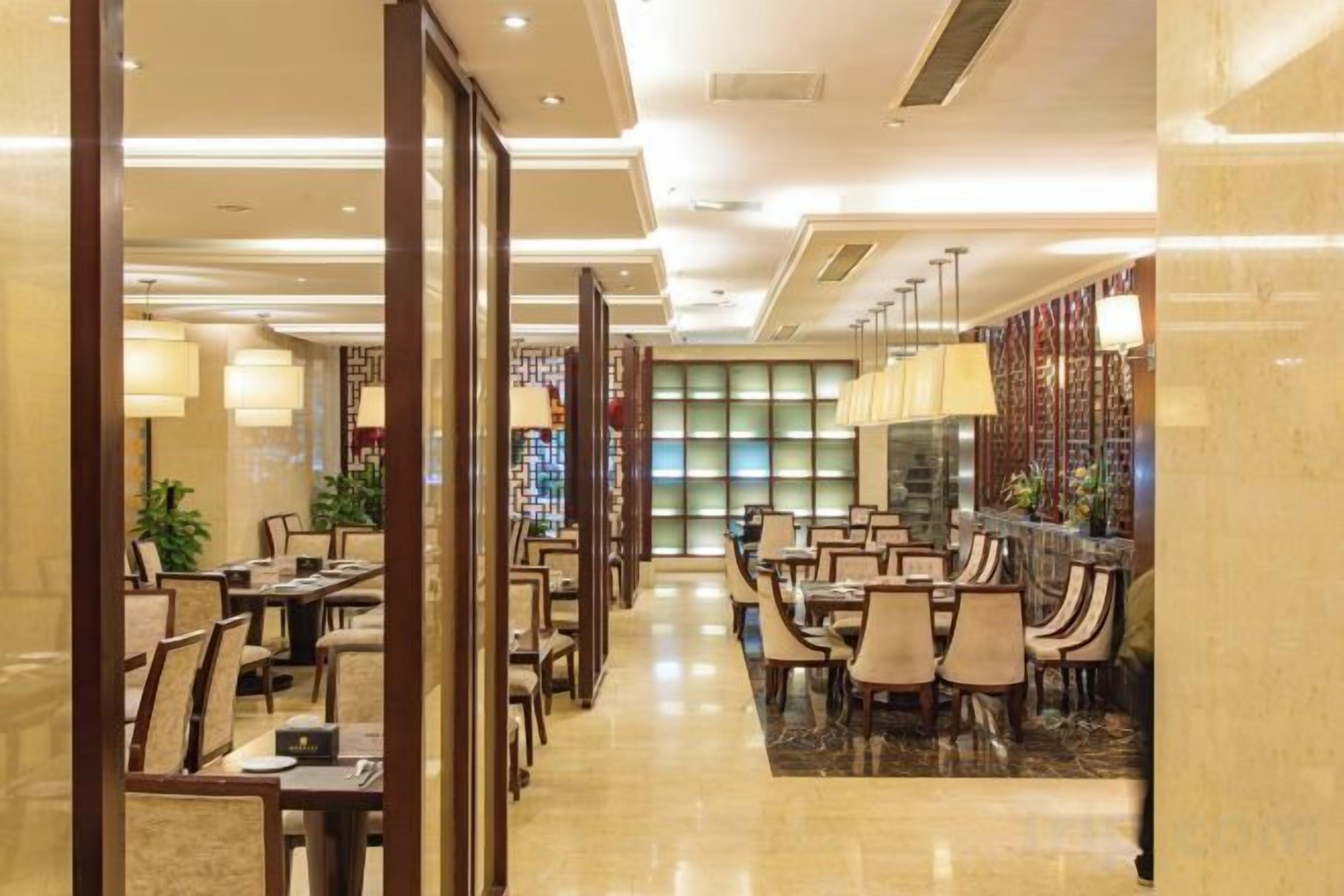 Eine Hotte Lobby mit einer langen Korridor, mehreren Esstischen und Stühlen sowie einem Barbereich mit einer gemusterten Wand.