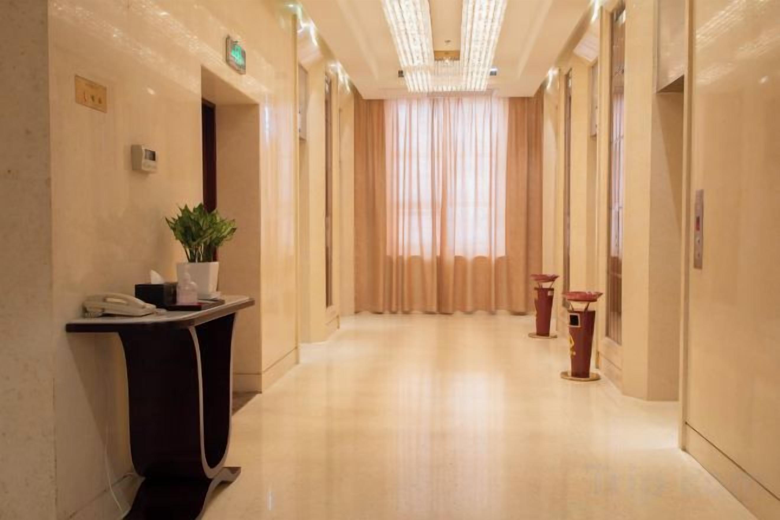 A hotel reception area with a reception desk, a potted plant, and a window with curtains.