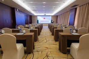 Une salle de conférence avec des rangées de tables et de chaises, un écran de projection à l’avant et un sol recouvert de moquette.