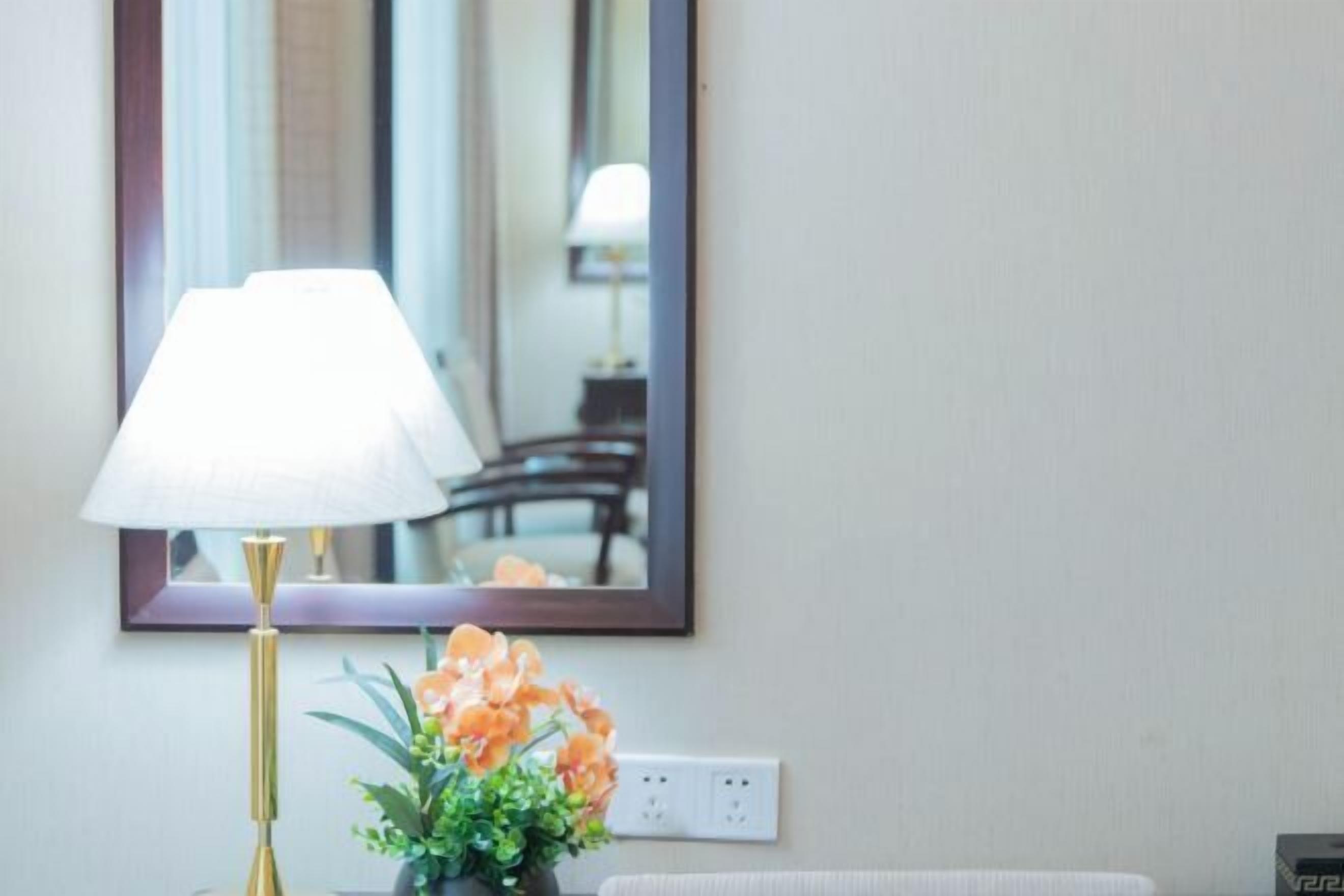 Ein Zimmer mit Nachttisch, Lampe, Spiegel und Blumenvase.
