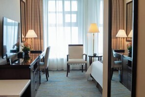 A hotel room with a bed, a desk, a chair, a lamp, and a large window with curtains. - Jiuzhou Tongqu Hotel (Wuhan)