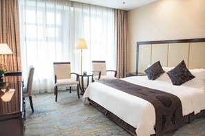 Une chambre d’hôtel avec un grand lit, deux chaises, un bureau et une lampe.