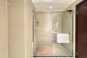 Un espace douche fermé par des parois de verre, doté d’un sol carrelé et d’une serviette blanche accrochée au mur.