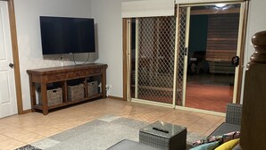 Un salon équipé d’un téléviseur, de meubles en osier, d’une porte-fenêtre coulissante et d’un sol carrelé.