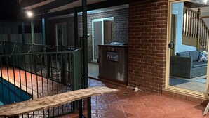 Un espace extérieur aménagé en terrasse, avec une piscine, un banc en bois et un mur en briques.