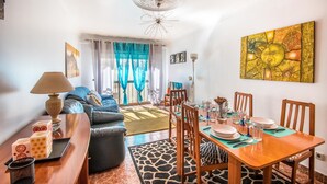 Una sala de estar moderna con un sofá, una mesa de comedor y sillas. Hay una lámpara en una mesita auxiliar y un cuadro en la pared.