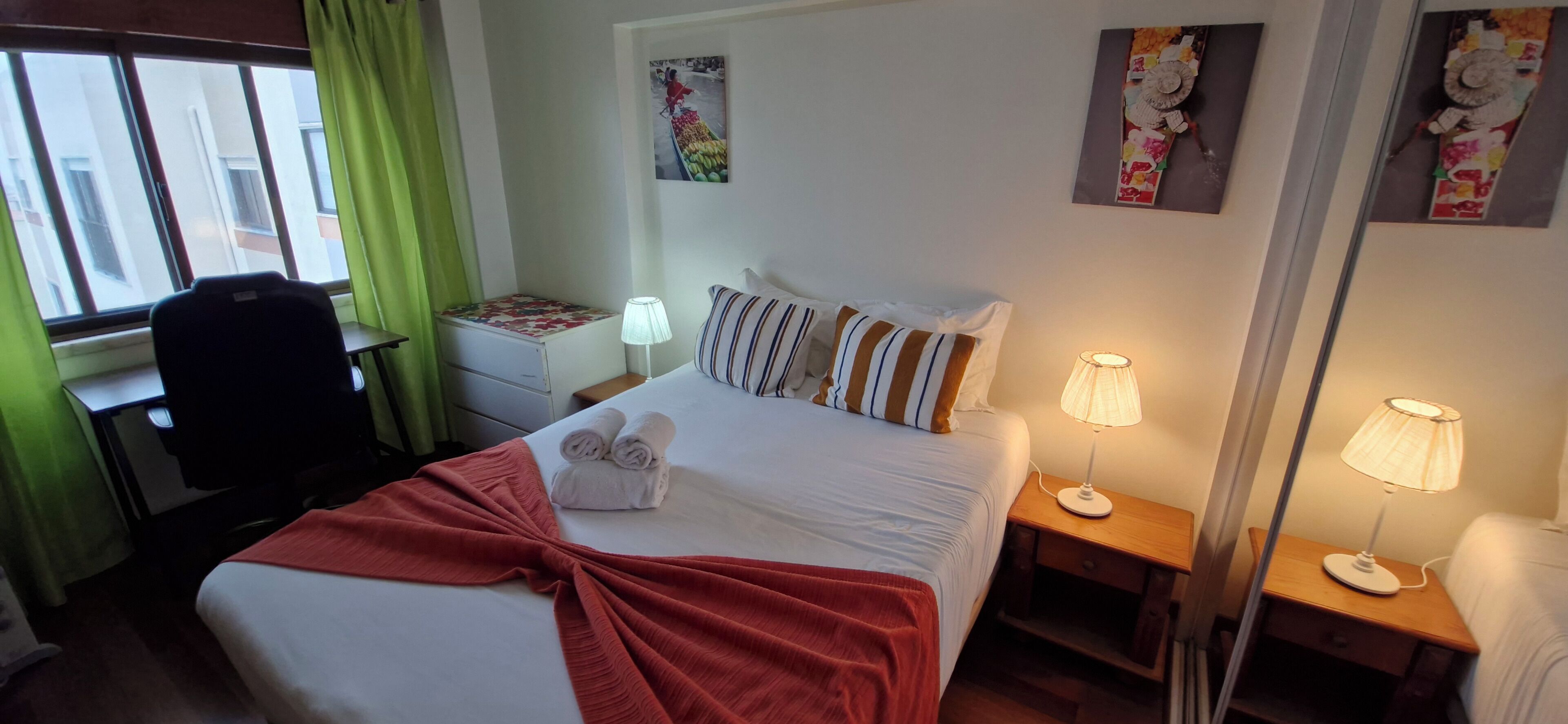 Une chambre d’hôtel avec un lit, deux tables de chevet, un bureau, une chaise et une fenêtre avec des rideaux.