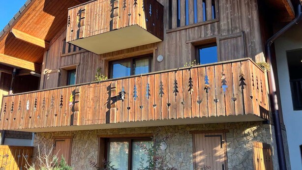 Un chalet en bois doté d’un balcon orné de motifs en forme de cœur et d’une façade en pierre.