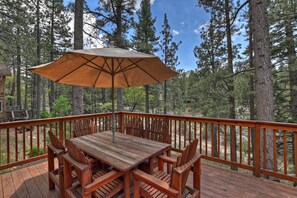 A wooden deck with a table and chairs, surrounded by a wooden railing, set in a forested area. - Chalet Yosemite: Air Conditioning! Amazing Moonridge Setting! Spa! Great Forest and Ski Slope Views! (Big Bear Lake)