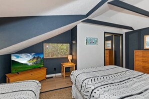 A bedroom with a sloped ceiling, a bed with patterned bedding, a TV on a wooden dresser, and a window with blinds. - Chalet Yosemite: Air Conditioning! Amazing Moonridge Setting! Spa! Great Forest and Ski Slope Views! (Big Bear Lake)
