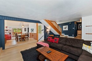 A spacious living area with a staircase, a dining area, and a kitchen visible in the background.