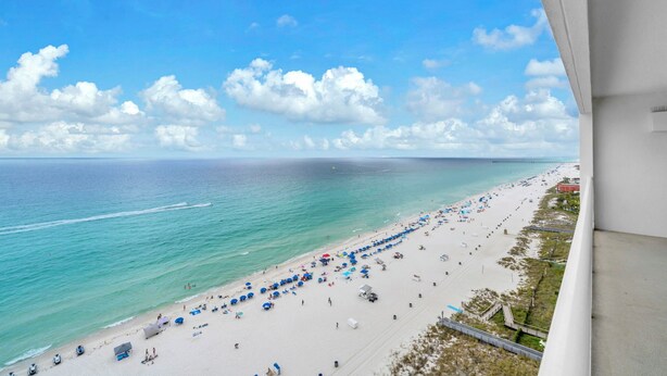 Blick auf einen Strand mit Sonnenschirmen, sandigem Ufer und blauem Himmel.