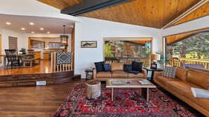 A spacious living area with a wooden ceiling, a large window overlooking a deck, a sofa set, and a coffee table.