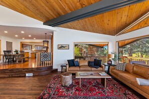 A spacious living area with a wooden ceiling, a large window, a leather sofa, and a patterned rug.