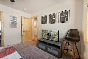 Ein Wohnzimmer mit Fernseher, einer Holztür und einem an der Wand befestigten Schild, das Annehmlichkeiten wie eine Skihütte und ein Pulterraum auflistet.