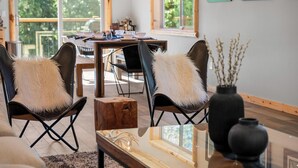 Un salon moderne avec deux fauteuils en cuir, une table basse en verre et un coin repas comprenant une table et des chaises en bois.