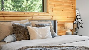 Une chambre à coucher avec une tête de lit en bois, un lit avec plusieurs oreillers, une couverture et un télescope posé sur une table de chevet.