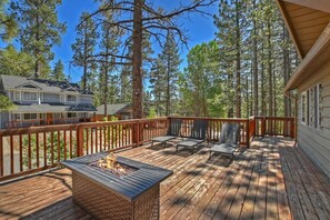 A wooden deck with a fire pit, outdoor furniture, and a view of a forested area.