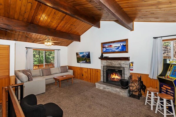 A cozy living room with a fireplace, a sofa, a coffee table, and a game console.