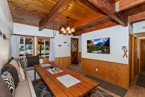 A wooden interior with a dining table, seating area, and a TV on the wall.