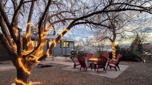 A backyard with a fire pit, red Adirondack chairs, and string lights wrapped around trees. - Denver Retreat • Hot tub+Firepit+Games • Fast Wifi (DENVER)