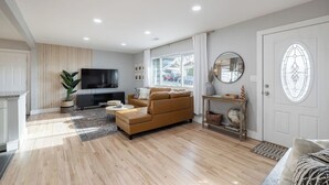 A modern living room with a sofa, TV, and a large window. - Denver Retreat • Hot tub+Firepit+Games • Fast Wifi (DENVER)