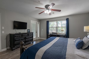A bedroom with a bed, a ceiling fan, a TV, a dresser, and a window with curtains.