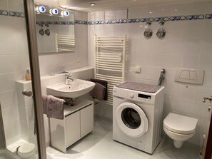 A modern bathroom with a sink, mirror, towel rack, washing machine, and toilet. - Fe apartm., in a quiet location, 5 minut. from the S-Bahn + Regio train station (Meckesheim)