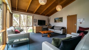 Un salon moderne doté d’une grande fenêtre, d’un téléviseur à écran plat, d’un canapé, d’une table basse et d’un plafond en bois.