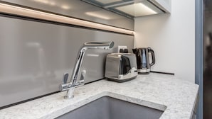 A modern kitchen with a stainless steel faucet, a toaster, and a coffee maker on a marble countertop. - Studio In the Lanes (Brighton)