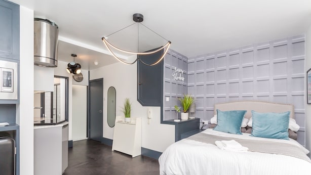 A modern bedroom with a large bed, a bedside table, a mirror, and a wall-mounted light fixture. - Studio In the Lanes (Brighton)