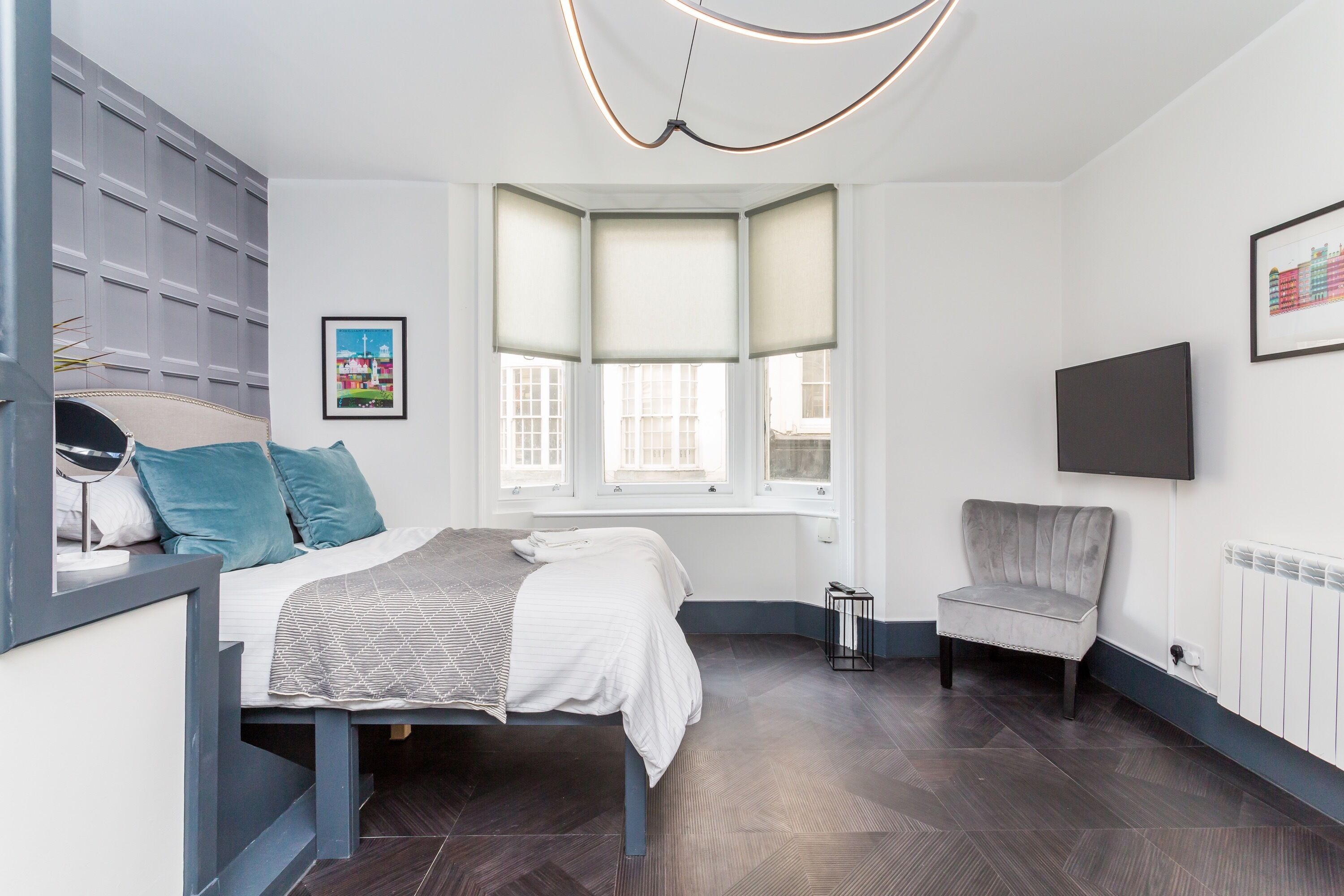 A modern bedroom with a bed, a chair, a desk, and a window with blinds.