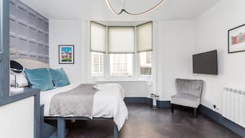 A modern bedroom with a bed, a chair, a desk, and a window with blinds.