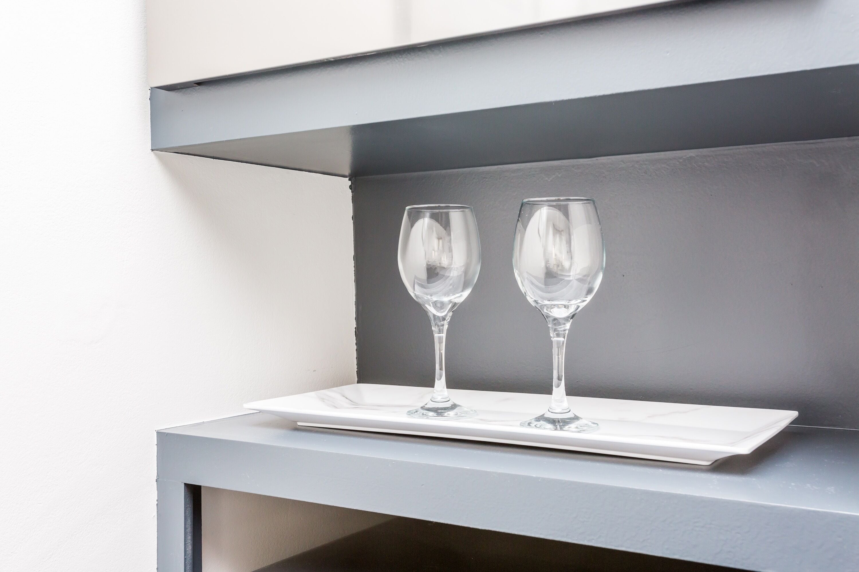 A white tray with two clear wine glasses on a grey surface.