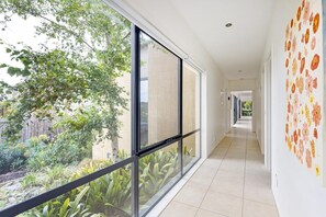 Un pasillo con amplios ventanales, piso de baldosas y un mural floral en la pared.