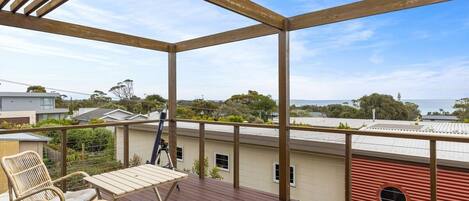 A wooden deck with a table and chairs, overlooking a residential area and the sea.