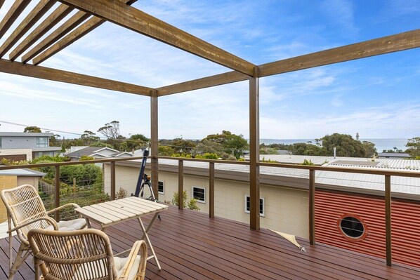 A wooden deck with a table and chairs, overlooking a residential area and the sea.