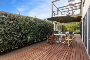 Una terraza de madera con mobiliario exterior, una pérgola y un seto.