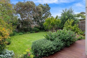 A well-maintained garden with a wooden deck, a lawn, and various shrubs and trees.