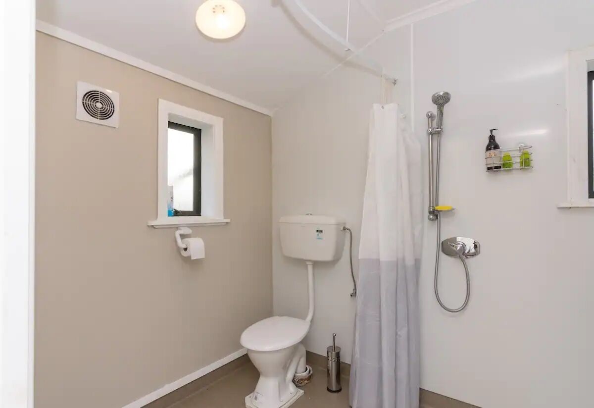 A bathroom with a toilet, a shower, a toilet paper holder, and a hand dryer.