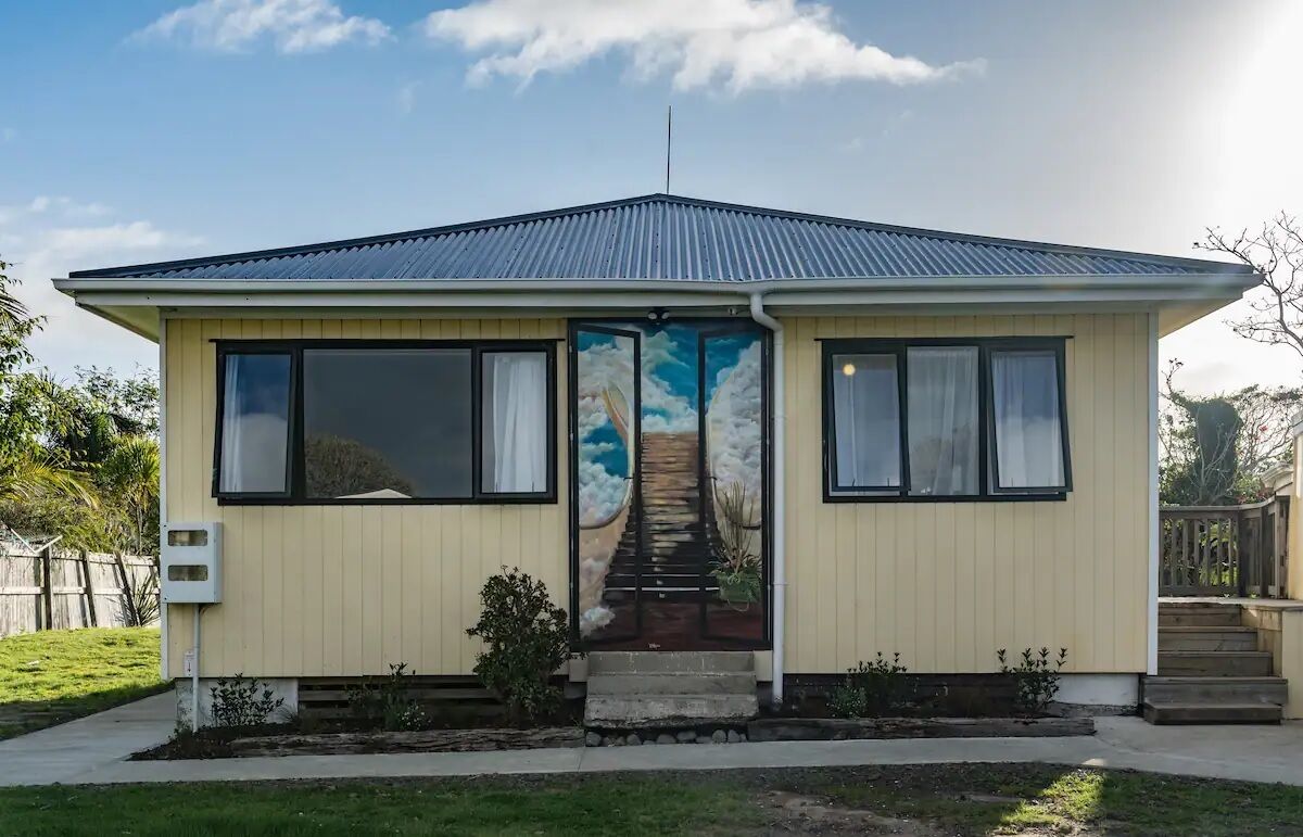 A single-story house with a gabled roof, a front door with a painted sky and clouds design, and a small front porch.