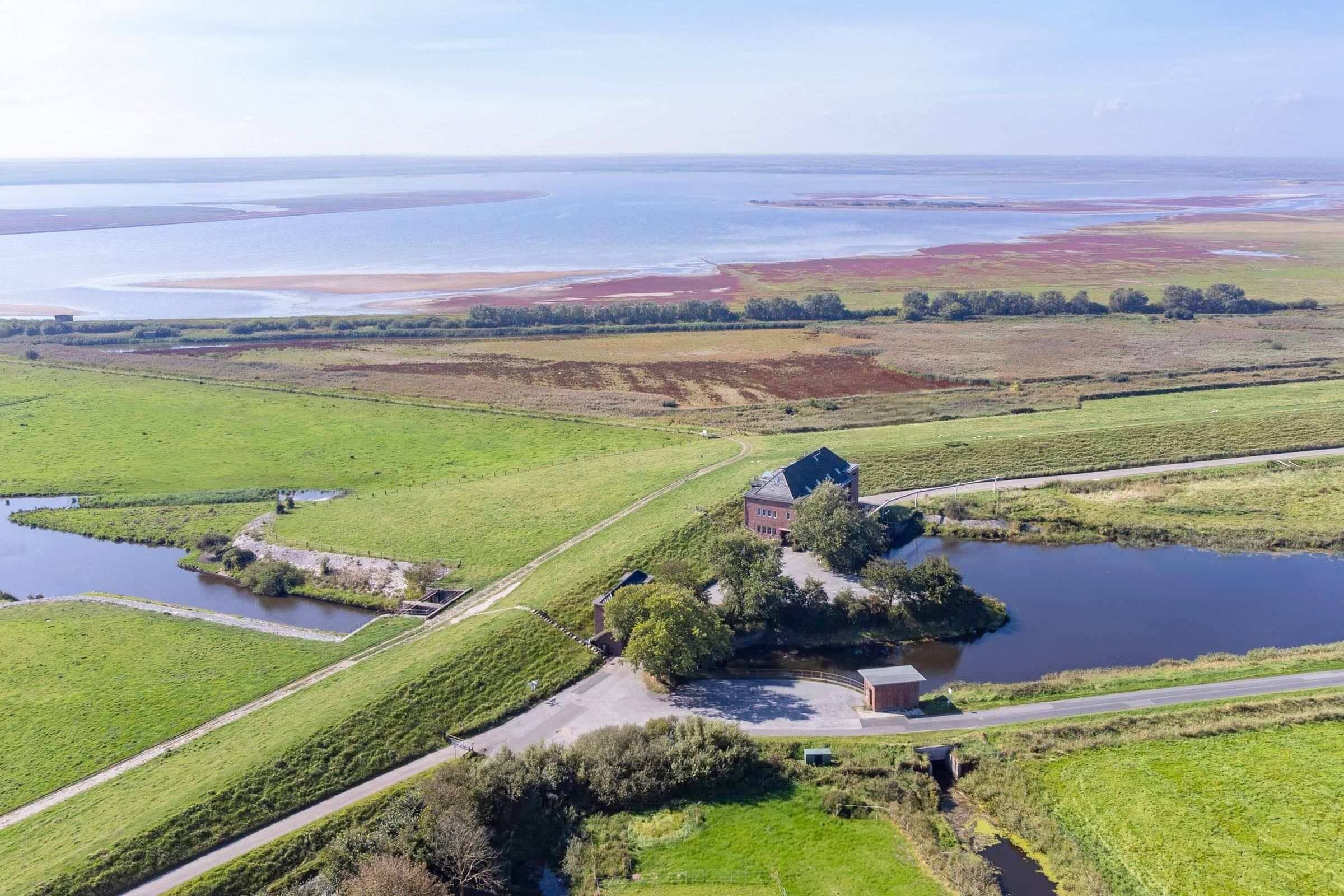 Vue aérienne d’une propriété rurale avec une grande maison entourée de champs verdoyants et de plans d’eau.