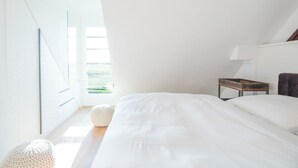 Quarto com uma cama grande, mesa de cabeceira, abajur e vista do exterior pela janela.