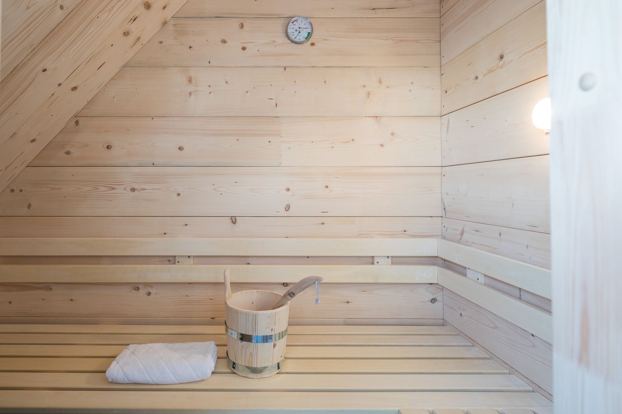 A wooden sauna with a bench, a bucket, and a towel.